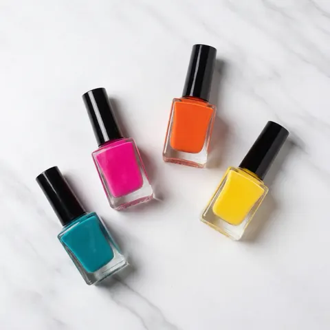 Vue de dessus de quatre flacons de vernis à ongles aux couleurs vives posés sur une surface en marbre blanc, idéal pour la promotion de produits de beauté et de manucure.