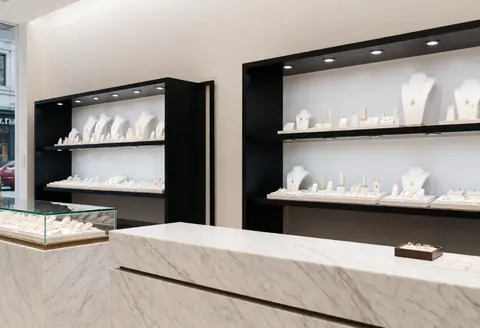 Intérieur d'une boutique de joaillerie moderne avec des vitrines en marbre blanc et des étagères noires, éclairage professionnel et bijoux exposés sur des présentoirs.