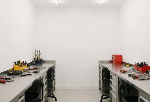 Atelier de réparation de téléphones avec tables en acier inoxydable, outils organisés et murs blancs, offrant un environnement propre et professionnel.