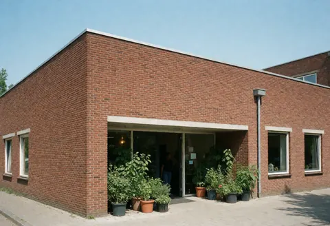 Façade moderne en briques rouges avec large entrée et plantes en pot sous un ciel clair, idéale pour les réunions et activités communautaires.