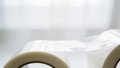 Rouleau de ruban adhésif transparent posé sur un fond blanc uni et flou, servant de support neutre pour ajouter du texte lié aux services de déménagement.