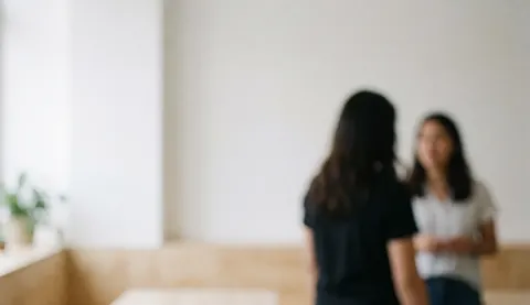 Deux personnes discutent dans un espace de coworking aux murs blancs et au mobilier en bois clair, dans une ambiance lumineuse et décontractée.