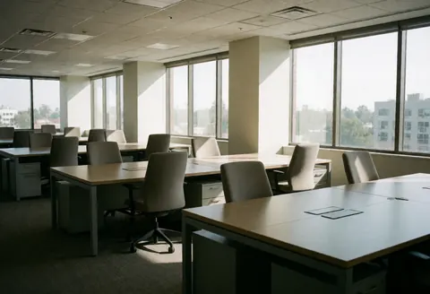 Espace de travail contemporain et désertifié, équipé de tables et de chaises, avec de grandes fenêtres laissant pénétrer la lumière du soleil matinal.