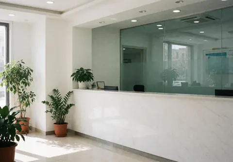 Intérieur d'une clinique médicale avec un comptoir blanc, des plantes vertes et des murs blancs, prêt à accueillir les patients.