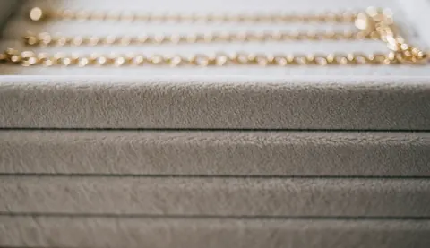 Fond de bijouterie avec texture de velours beige et chaînes dorées floues, idéal pour textes et design web.