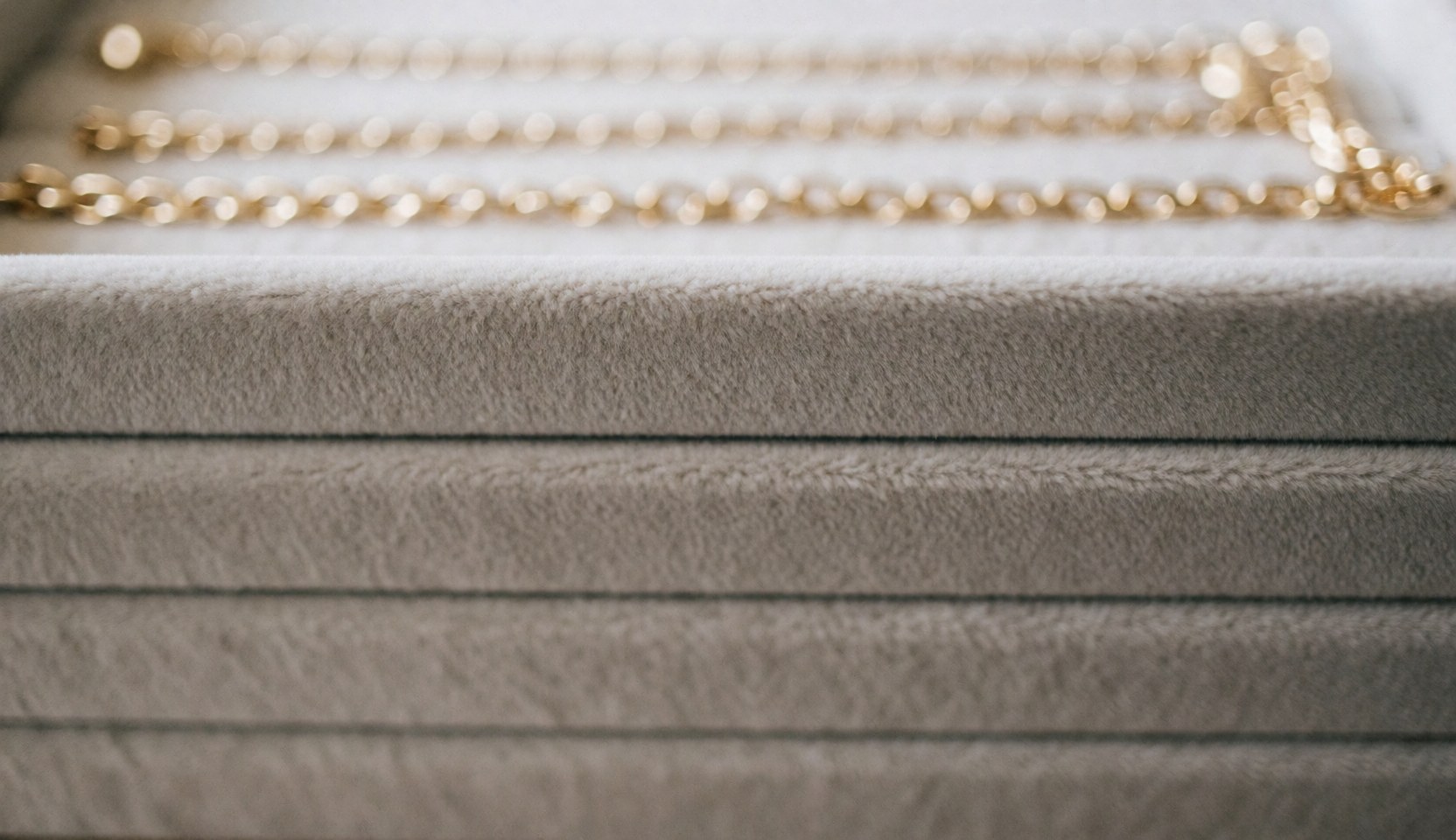 Fond de bijouterie avec texture de velours beige et chaînes dorées floues, idéal pour textes et design web.