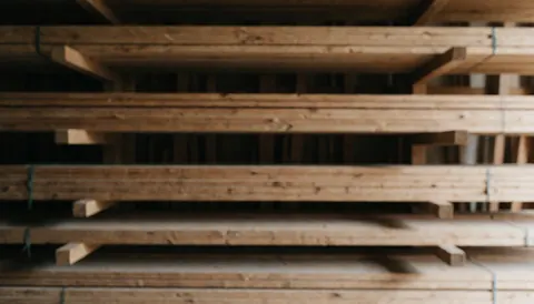 Piles de planches de bois empilées dans un entrepôt de menuiserie avec un fond flou et chaleureux, idéal pour ajouter du texte.