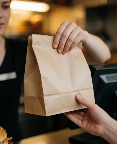 Une caissière remet un sac contenant de la nourriture rapide à un client derrière le comptoir, dans un environnement chaleureux et accueillant.