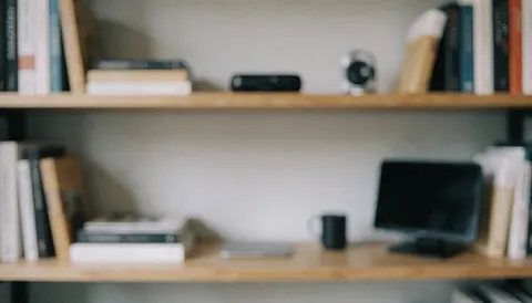 Étagère en bois contenant des livres, un ordinateur, un téléphone portable et des accessoires technologiques sur un fond flou adapté aux textes.