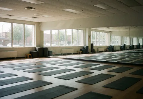 Un studio de yoga vide présentant des couvertures bien rangées, des miroirs et des fenêtres laissant entrer la lumière naturelle pour un environnement calme et propre.