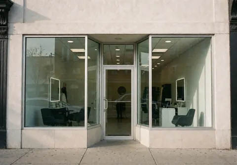 Façade d'un salon de toilettage pour chiens avec fenêtres en verre, entrée principale et chaises visibles à l'intérieur, ambiance propre et professionnelle.