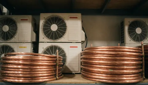 Vue de tuyaux de cuivre enroulés et d'unités de climatisation sur des étagères dans un environnement industriel avec une texture réaliste.