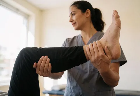 Femme fisiothérapeute effectuant un étirement de jambe sur un client en consultation, dans un cadre professionnel et lumineux, adapté aux services de santé et de bien-être.