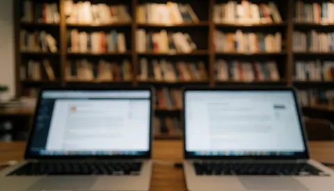 Deux ordinateurs portables aux écrans flous devant des étagères remplies de livres, idéal pour ajouter du texte ou des en-têtes sur un site web.