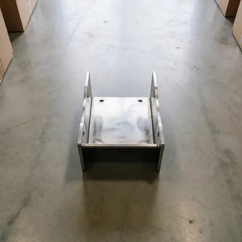 Un support métallique poli et robuste repose sur un sol en béton dans un entrepôt, avec une lumière diffuse qui met en valeur son fini industriel.