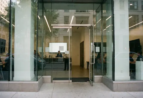 Façade vitrée d'entrée de bureau avec personnes travaillant à l'intérieur, ambiance professionnelle et épurée, idéale pour startups et entreprises technologiques.