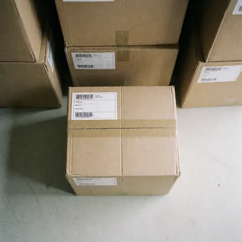 Carton de déménagement fermé et étiqueté, prêt à être expédié, dans un entrepôt avec d'autres cartons empilés, idéal pour les services de logistique.