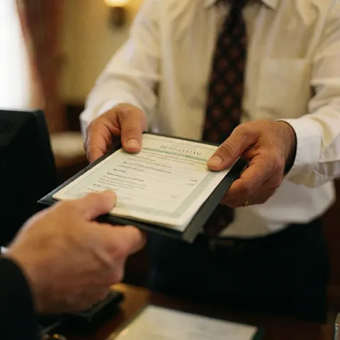 Un homme remet un document de voyage à un client dans une agence, mains et torse visibles, éclairage chaleureux, interaction professionnelle.
