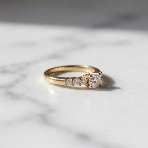 Une bague en or ornée de diamants brillants posée sur une surface en marbre, éclairée par une lumière latérale douce qui accentue l'éclat des pierres précieuses.
