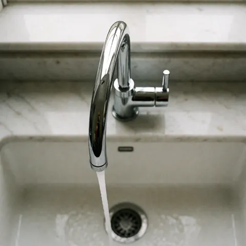 Un évier de cuisine équipé d'un robinet en chrome brillant avec de l'eau qui coule, posé sur un plan de travail en marbre blanc poli, dans une scène moderne et propre.