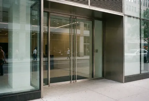 Façade en verre reflétant la rue, entrée accueillante d'un bureau urbain au design minimaliste et professionnel.