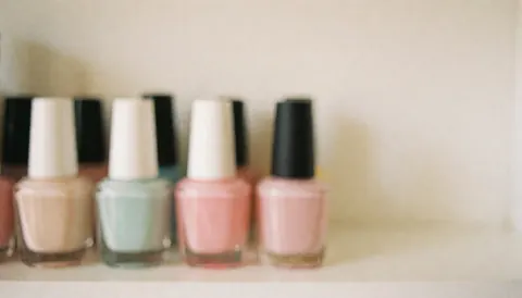 Des flacons de vernis à ongles aux couleurs pastels disposés sur une étagère, offrant un fond doux et uniforme idéal pour ajouter du texte.