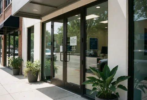Façade vitrée d'un magasin de services informatiques avec des plantes en pot et des reflets de la rue sur les portes.