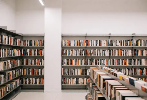 Vue intérieure d'une librairie contemporaine dotée de rayonnages métalliques chargés de livres, sur fond de murs blancs et de sol clair.