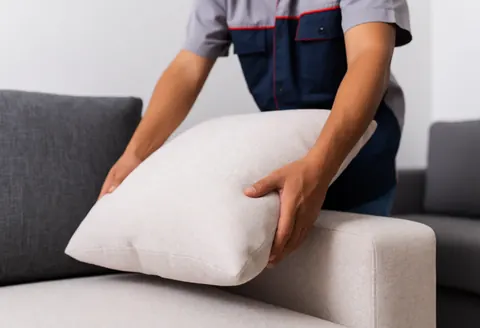 Un homme ajuste un coussin sur un canapé en tissu dans une boutique de meubles, illustrant le service client avec une lumière douce et réaliste.