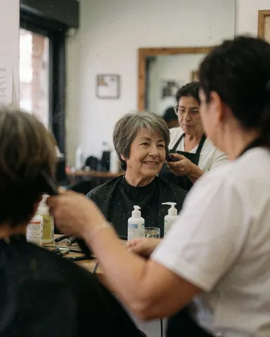 Une cliente sourit en admirant sa nouvelle coiffure dans le miroir pendant que la coiffeuse travaille.