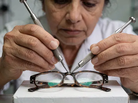 Un technicien ajuste minutieusement les vis d'une monture de lunettes à l'aide d'outils métalliques dans un environnement professionnel.