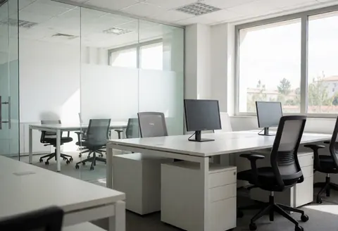 Espace de travail contemporain équipé de tables blanches, de chaises ergonomiques et de grandes fenêtres laissant entrer la lumière naturelle.