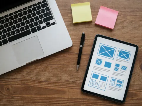 Ordinateur portable, tablette avec maquettes, post-it et stylo sur table en bois, scène professionnelle pour développement logiciel.