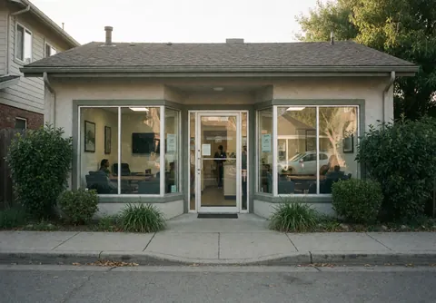 Façade d'auto-école avec entrée et vitres propres, montrant l'intérieur avec personnes et mobilier, entourée de végétation et de pavement.
