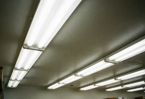 Éclairage fluorescent au plafond d'un entrepôt industriel, illuminant l'espace de travail avec des tubes lumineux.