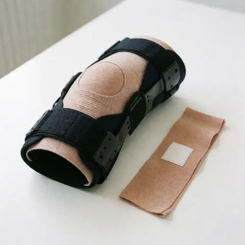 Une genouillère noire et un bandage rose posés sur une surface blanche, utilisés pour la rééducation physique et le soin des articulations.