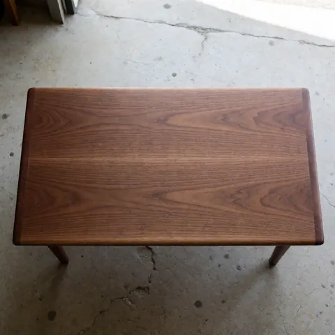 Vue d'une table en bois massif à la surface polie reposant sur un sol en béton fissuré, mettant en valeur la texture naturelle du matériau.