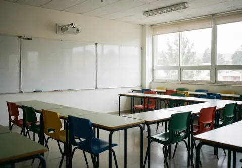 Salle de classe de langues vide équipée de chaises colorées et d'un tableau blanc, baignée de lumière naturelle par de grandes fenêtres, offrant un environnement propre et accueillant.