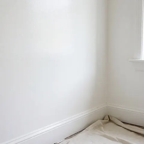 Mur intérieur blanc récemment peint, orné d'une moulure décorative en haut, avec une bâche de protection posée au sol pour éviter les taches.
