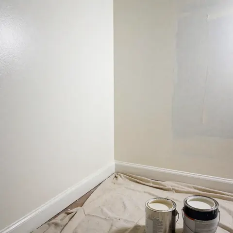 Mur intérieur fraîchement peint avec une toile posée contre lui et des boîtes de peinture, montrant un résultat propre et professionnel.