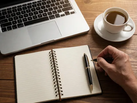 Bureau en bois avec un ordinateur portable, un cahier ouvert, un stylo et une tasse de café, idéal pour les cours en ligne ou le travail à distance.