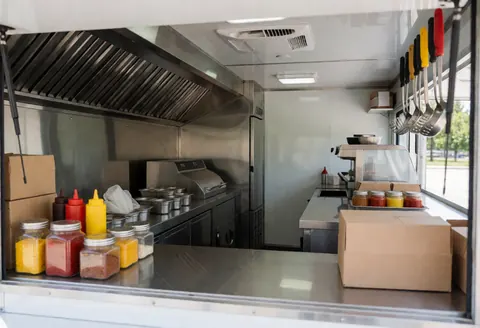 Intérieur propre d'un food truck avec comptoir en acier inoxydable, condiments, ustensiles suspendus et équipement de cuisine prêt pour la préparation.