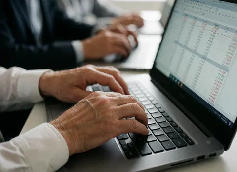 Gros plan sur des mains adultes utilisant un ordinateur portable affichant une feuille de calcul financière dans un bureau professionnel.