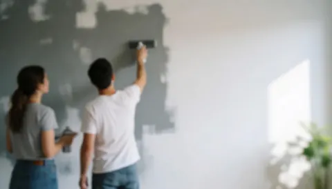 Un couple utilise un rouleau et un pinceau pour peindre un mur dans une pièce baignée de lumière naturelle.