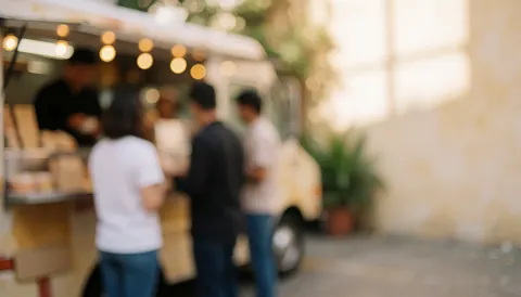Dos de clients commandant devant un food truck avec un arrière-plan flou chaud en extérieur.
