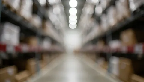 Vue floue d'une allée d'entrepôt bordée de rayonnages métalliques, éclairée par des lumières diffusant un effet bokeh abstrait sur le fond.