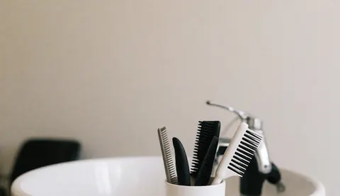 Divers brosses et peignes pour chiens disposés sur un lavabo blanc avec robinet dans un salon de toilettage animalier professionnel.