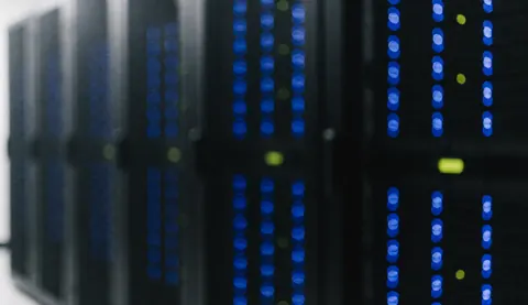 Des serveurs dans une salle de serveurs avec des lumières bleues et vertes allumées, créant un fond technologique flou idéal pour du texte.