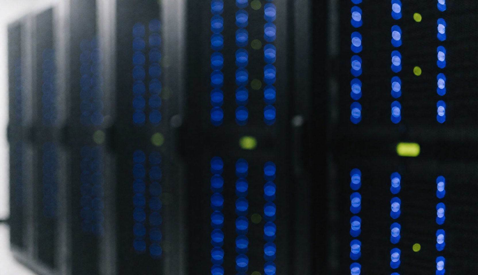 Des serveurs dans une salle de serveurs avec des lumières bleues et vertes allumées, créant un fond technologique flou idéal pour du texte.