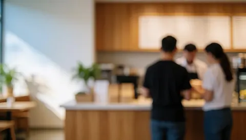 Deux clients passent une commande de café au comptoir en bois d'un établissement moderne baigné de lumière naturelle.